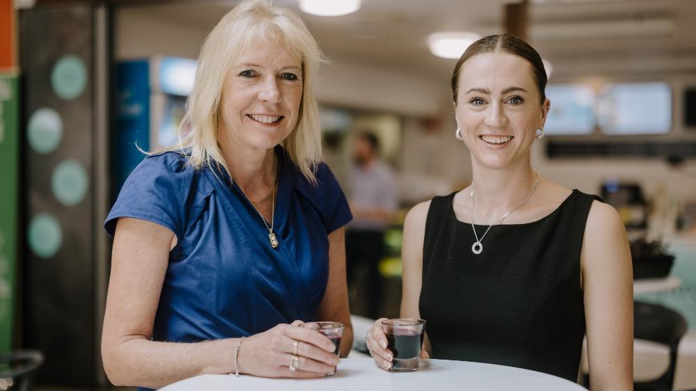 Karen Charlton and Denelle Cosier stand at a table, each with a glass of blackcurrant juice. Photo: Michael Gray