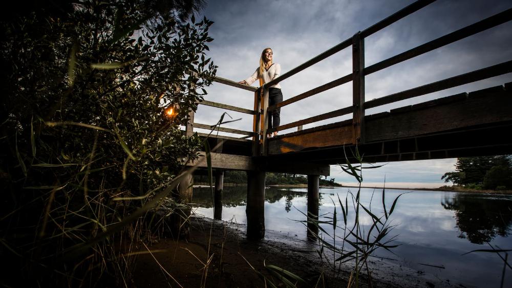 A female stands on a boardwalk looking out over a mangrove-laden coastline. Photo: Paul Jones