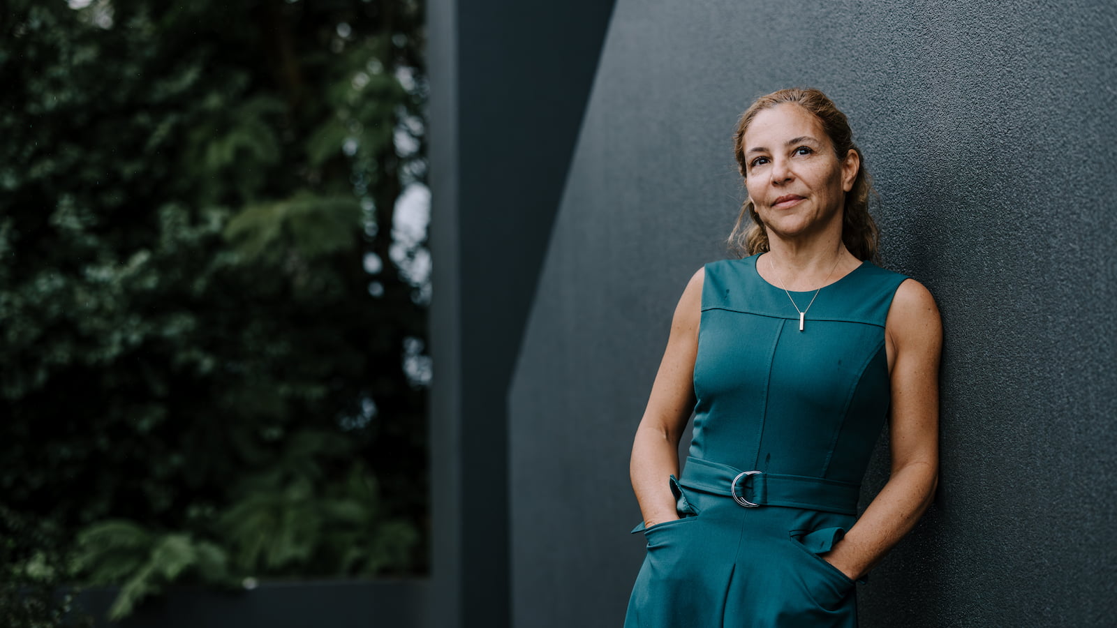 A woman with her hands by her side wearing a green dress stands in front of a building. Photo: MIchael Gray