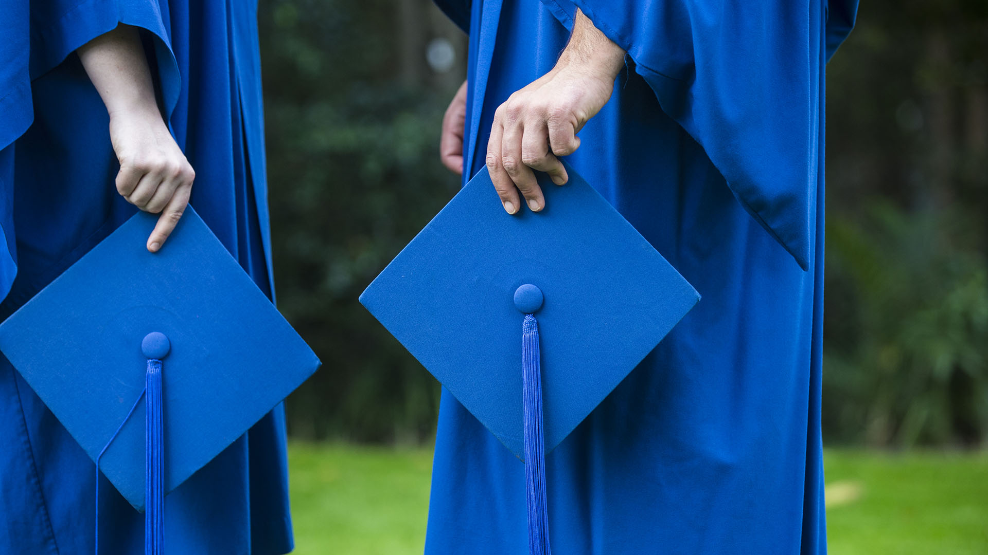2 UOW marketing students in academic gowns and holding mortarboards