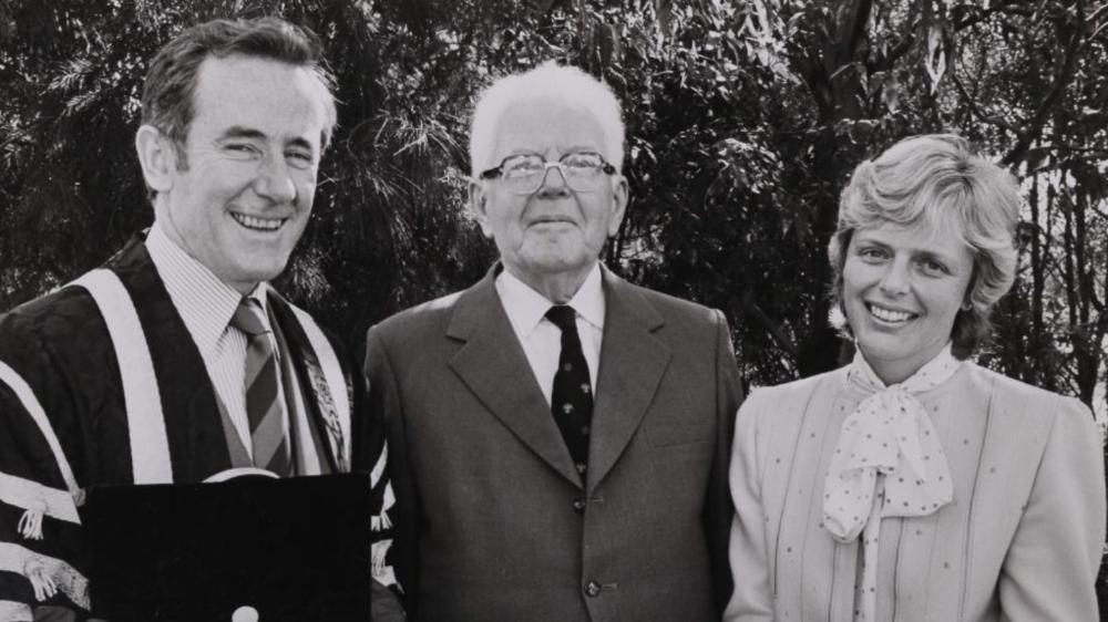 A black and white photo of Ken McKinnon and Sue Walker with Sir Mark Oliphant after a graduation ceremony in 1983