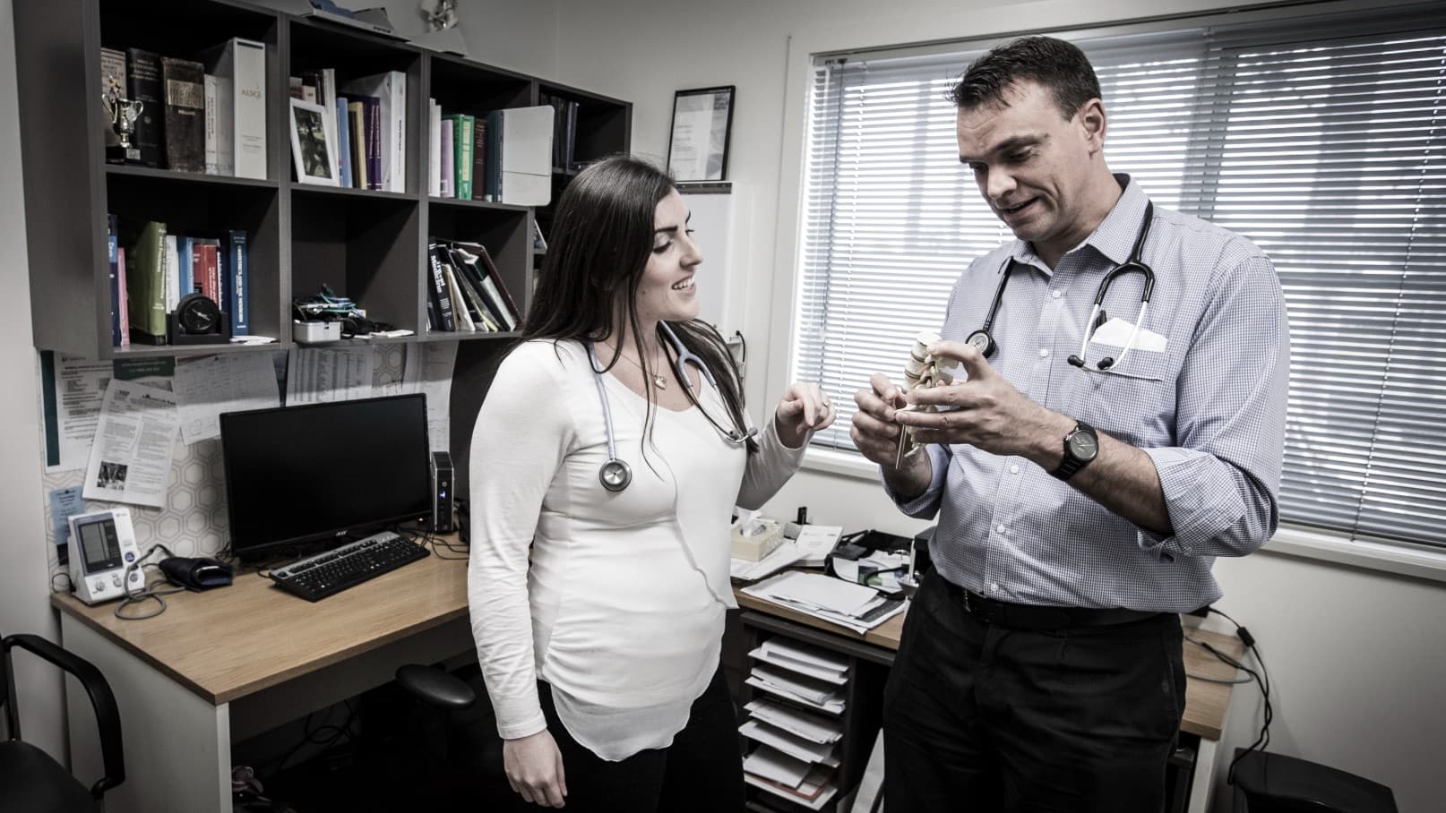 Two GPs, a female and male, stand in a doctors