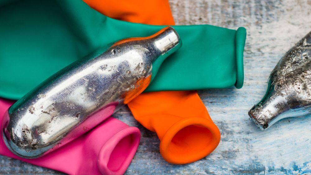 A nitrous oxide cannister sits on top of coloured deflated ballons