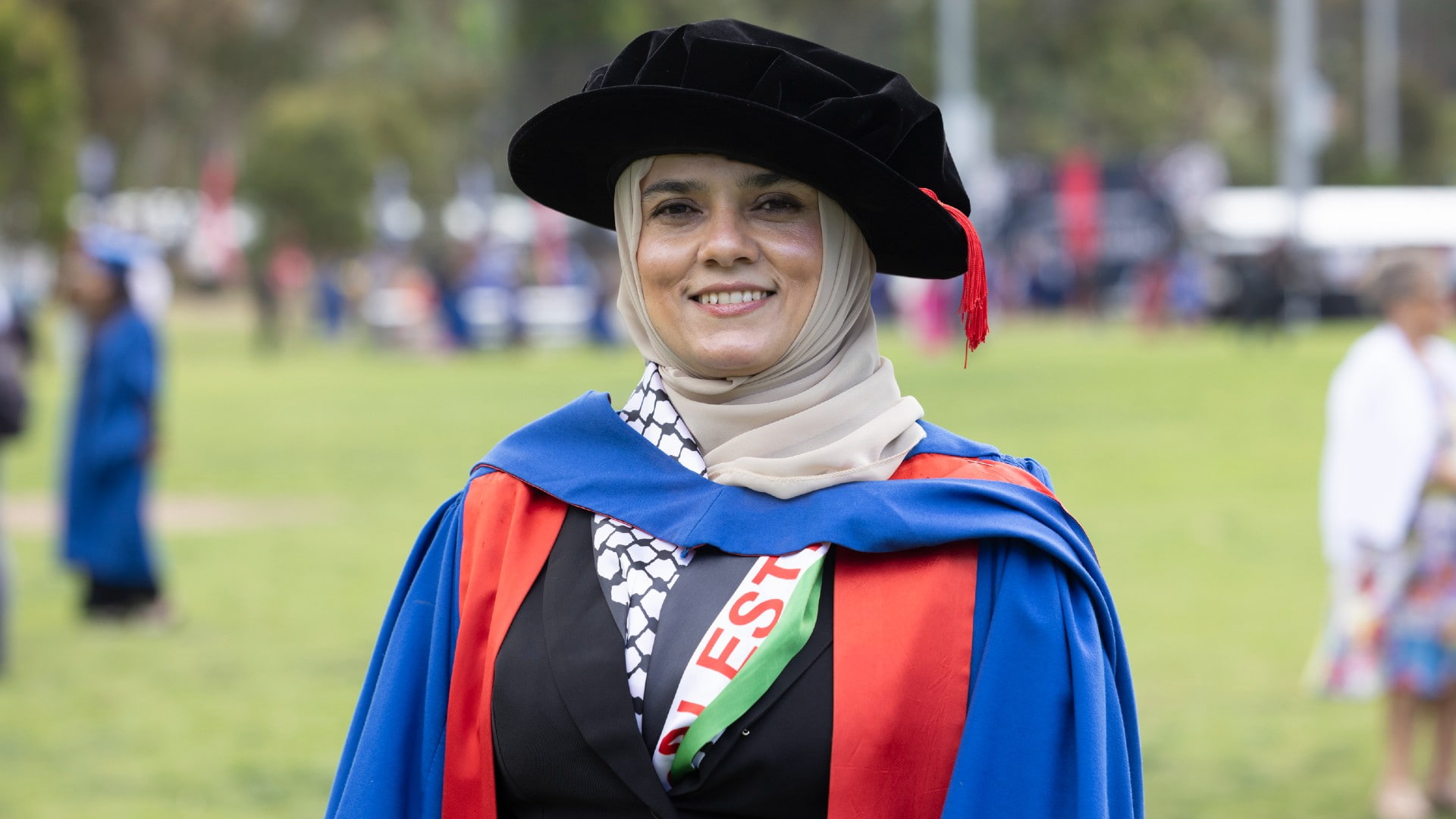 Dr Noor Jarbou wears a black graduation cap and blue and red gown. She smiles at the camera. Photo: Mark Newsham
