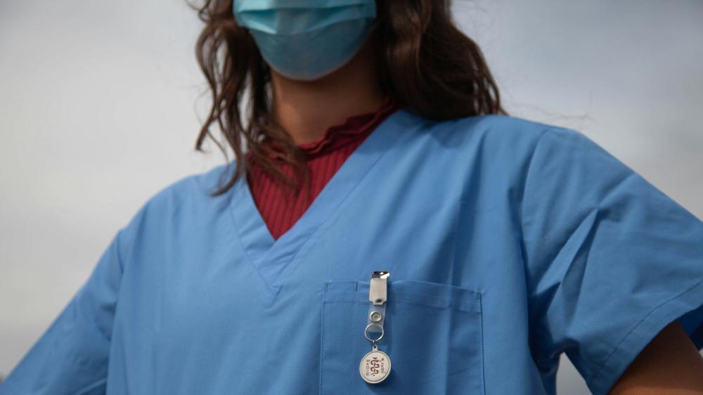 A person wearing medical scrubs with a medic alert badge visible on their shirt