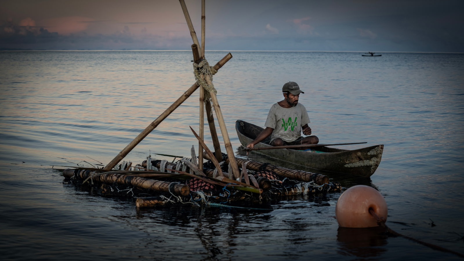 A man fishes from a traditional wooden canoe as it drifts in the ocean. The sun is rising behind the fisherman. Photo: Paul Jones