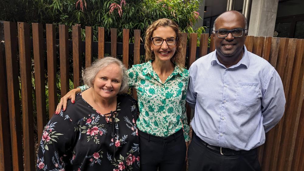Three people stand in a row, against a wooden fence. Photo: Clare Rhodes