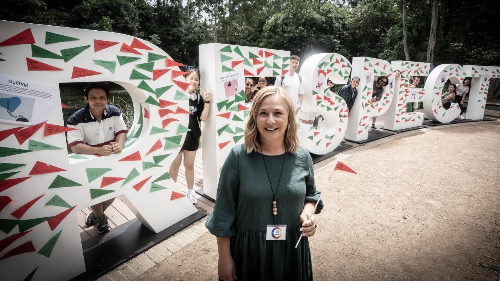 Angela Cowan stands in front of the Respect letters, with students in the background. She holds a red flag. Photo: Paul Jones