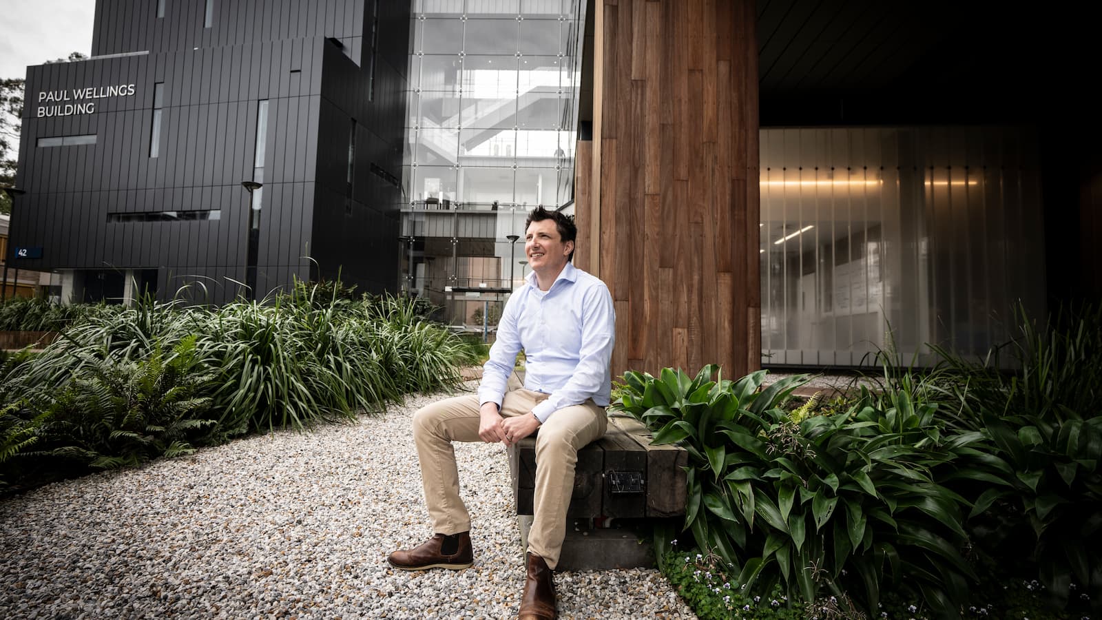 Dr Shane Ellis sits on a bench, surrounded by gardens, outside of the Molecular Horizons Building. Photo: Michael Gray