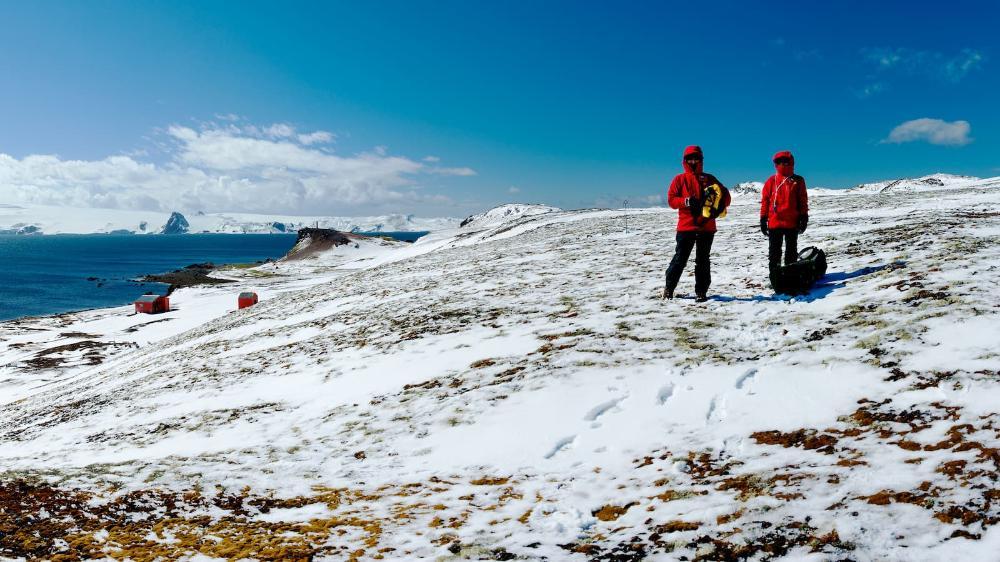 Two women wearing red protective snow gear stand in the snow in Antarctica. Photo: Andrew Netherwood