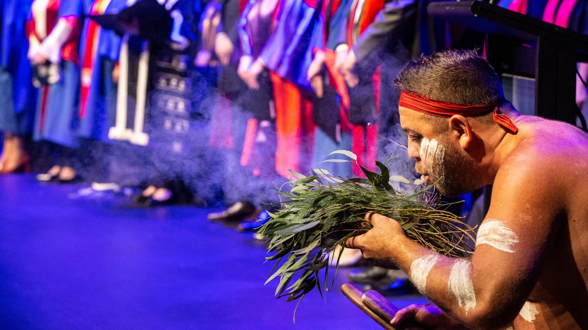 An Aboriginal man performs a smoking ceremony on stage at the UOW Shoalhaven graduations. Photo: Paul Jones