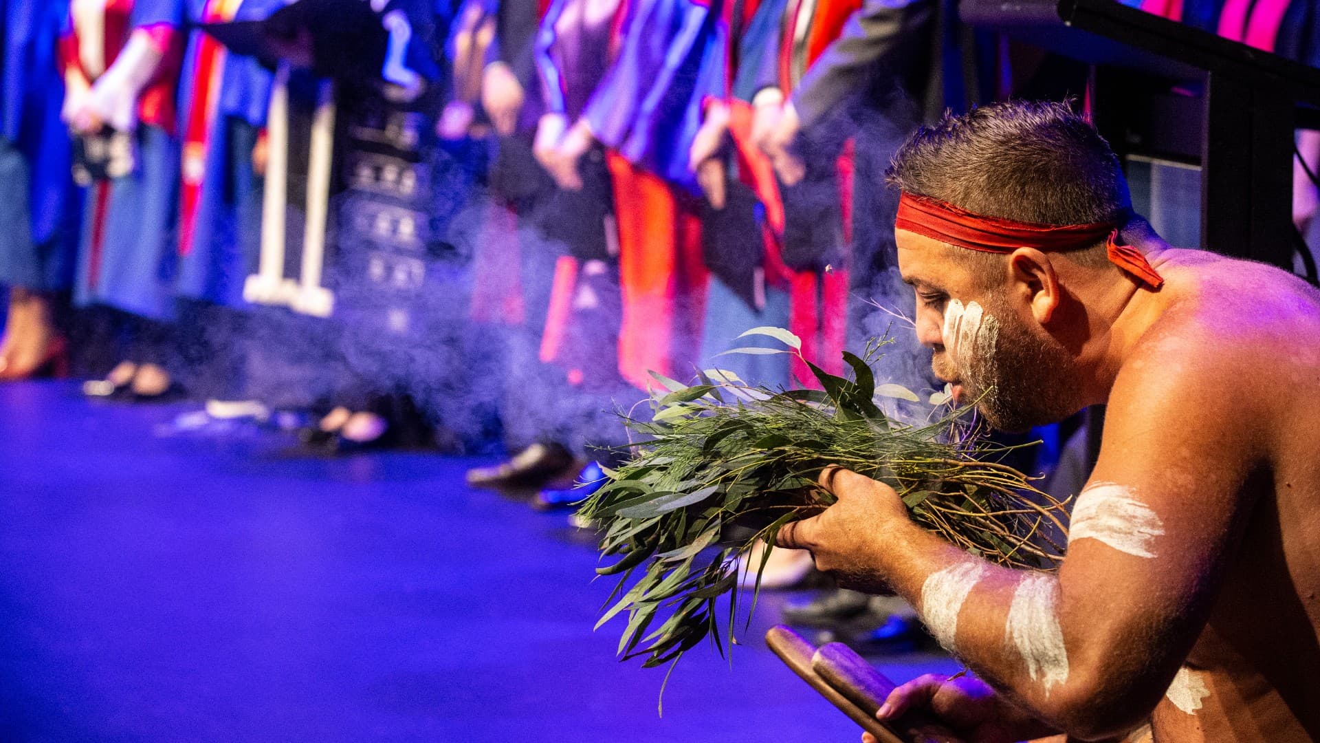 An Aboriginal man performs a smoking ceremony on stage at the UOW Shoalhaven graduations. Photo: Paul Jones