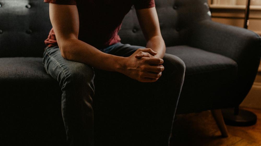 A person sitting on a sofa with clasped hands.