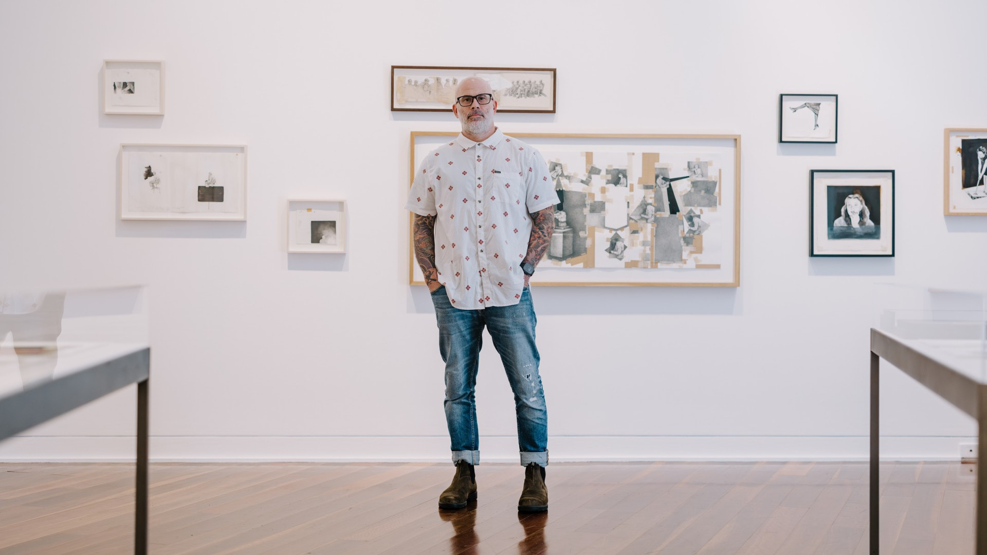 A man stands in a light-filled gallery with framed pictures on the wall behind him. Photo: Michael Gray