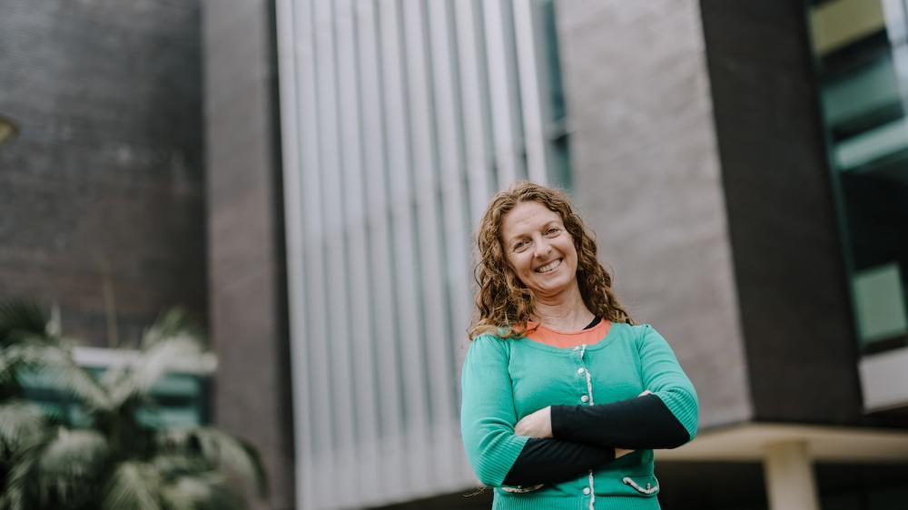 A woman with her arms crossed stands in front of a tall building. Photo: Michael Gray