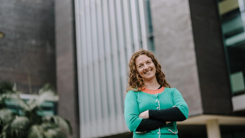 A woman with her arms crossed stands in front of a tall building. Photo: Michael Gray