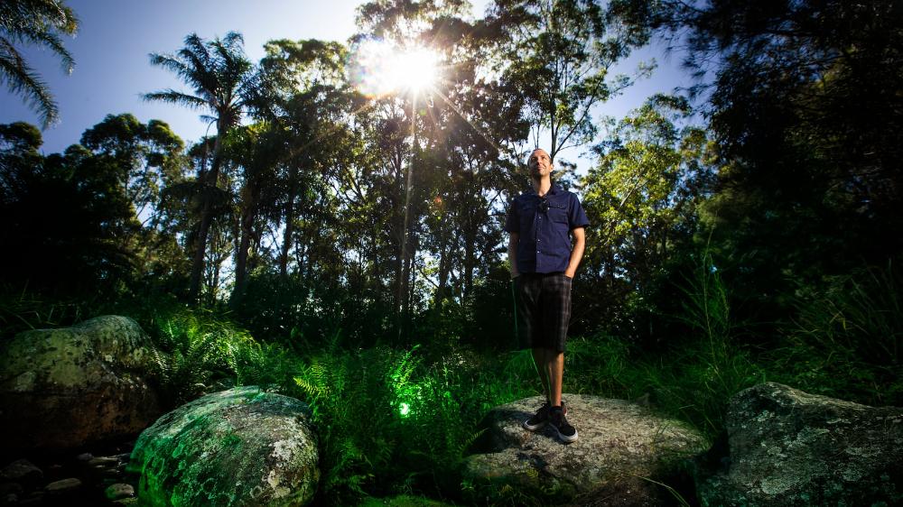 A man stands on a rock in a lush garden landscape at UOW's Wollongong Campus. Photo: Paul Jones