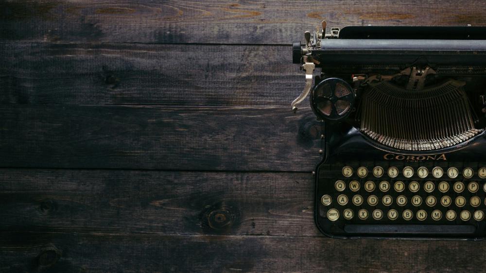 A black old-fashioned typewriter sits on a rustic wooden table