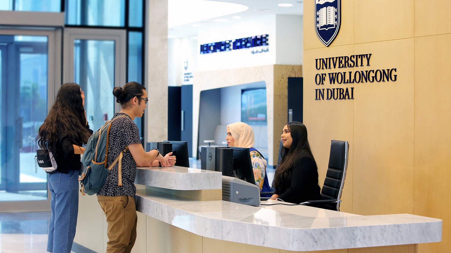 A student and staff member interact at the information desk at UOW Dubai campus.