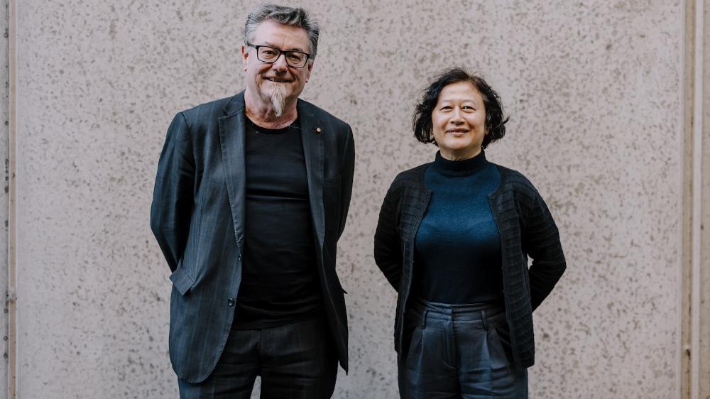 A man and a woman smile and stand in front of a wooden wall. Photo: Michael Gray