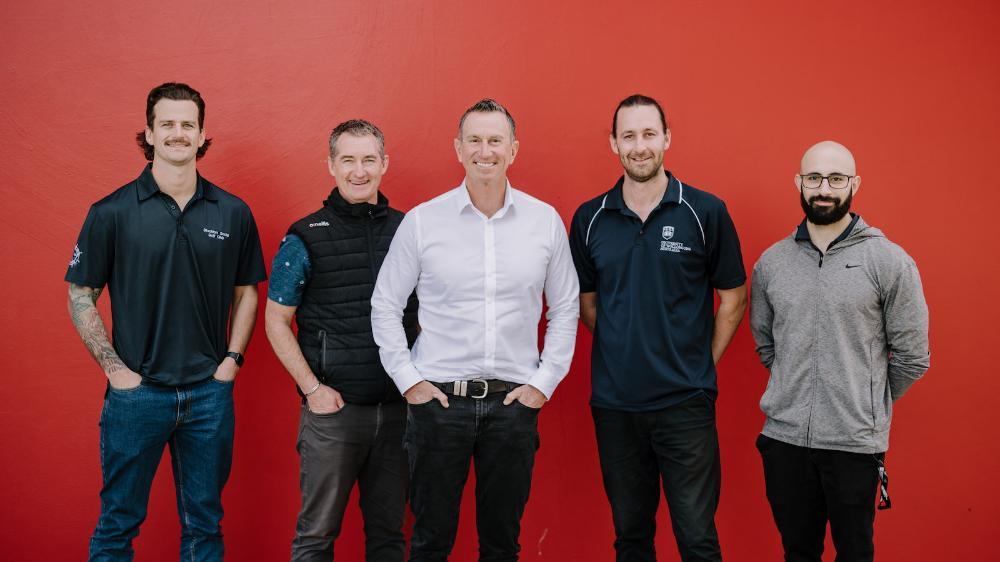Five people stand in a row in front of a red background. Photo: Michael Gray