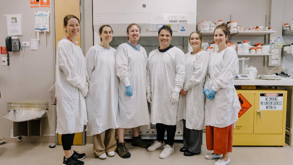 Six people in white lab coats stand in a row in a science lab. Photo: Michael Gray