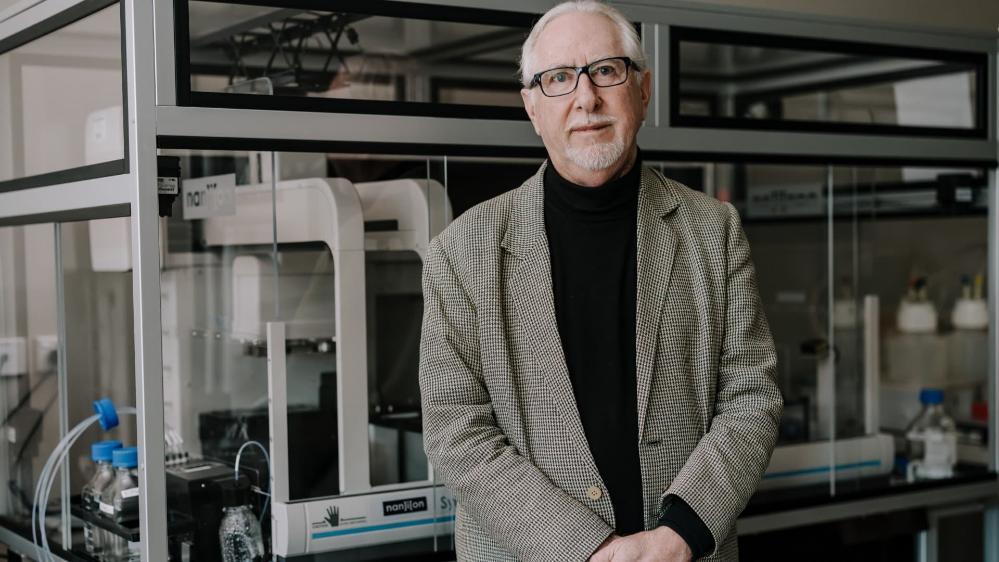A man stands in front of a microscope in a lab setting. Photo: MIchael Gray