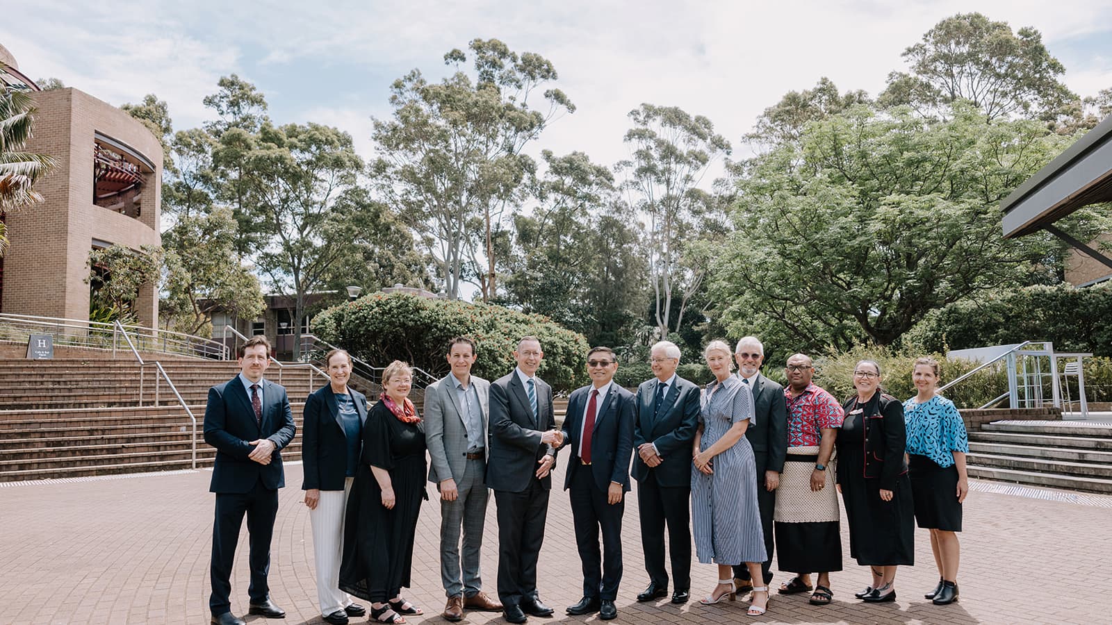 A group of people, both men and women, stand in a row outside a building on UOW's Wollongong Campus with gum trees in the background. Photo: Michael Gray