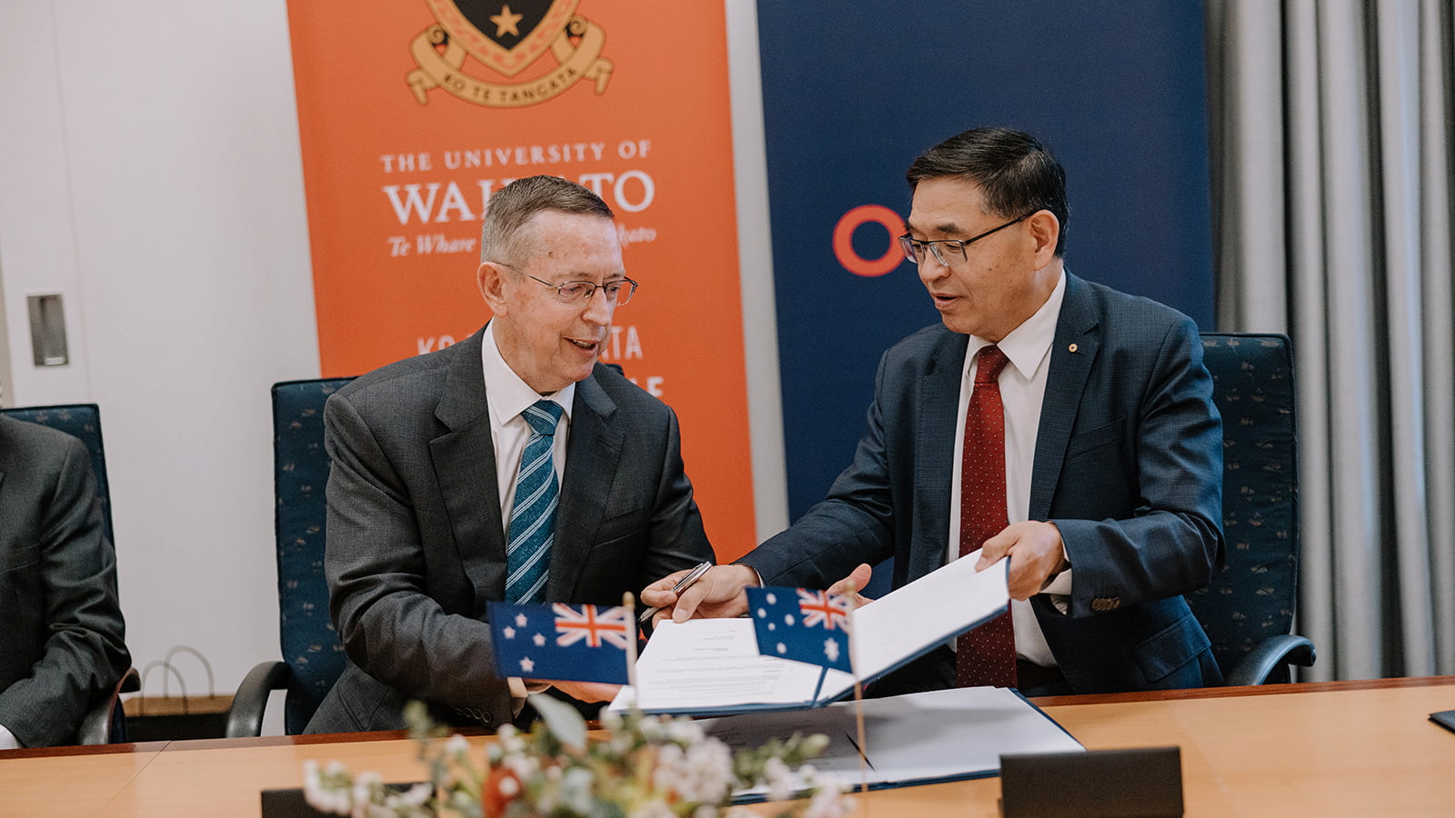Two men shake hands in a large boardroom after signing documents together. They are both wearing suits and ties. Photo: Michael Gray