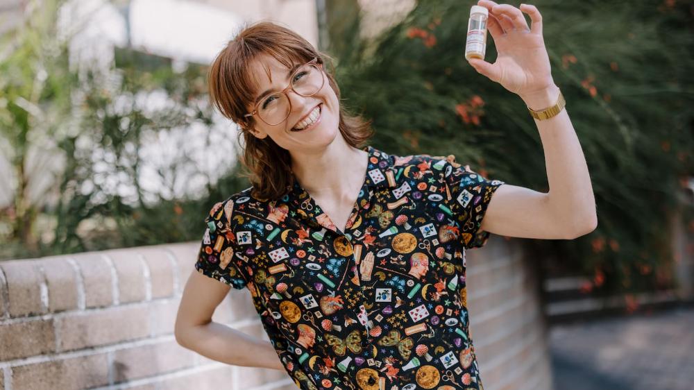 Alice O'Keefe has a big smile and stands in front of the Molecular Horizons Building. She is holding a small test tube. She wears jeans, a black shirt, and glasses. Photo: Michael Gray