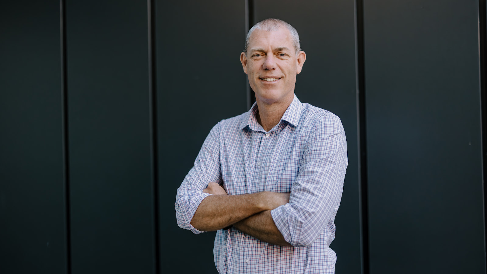 A man stands in front of a black background with his arms crossed. Photo: Michael Gray