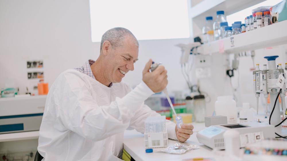 A man in a white lab coat sits at a laborary bench. Photo: Michael Gray