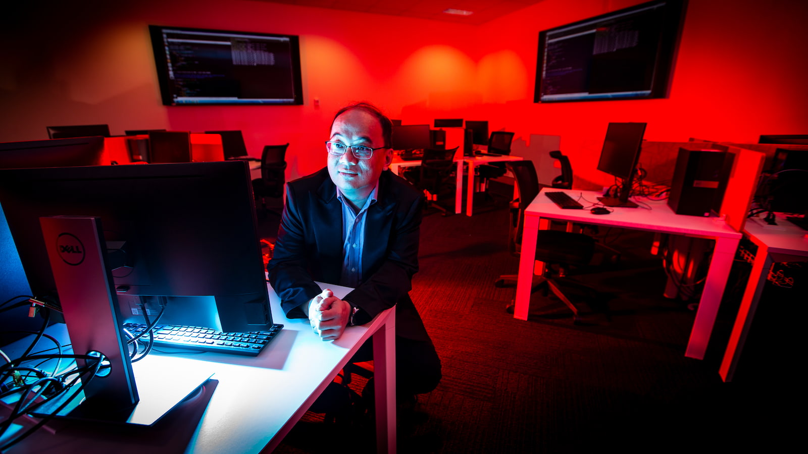 A man sits in front of a computer in a room with lots of red light. Photo: Paul Jones