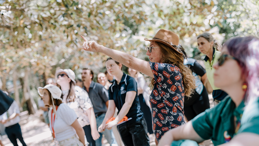 A woman in a floral dress with a straw hat Alison Scobie pointing up at the tree canopy