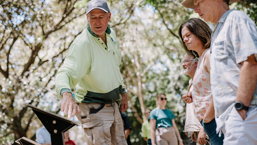 Anthony Wardle in hi-vis, pointing at one of the campus tree walk signs and showing some spectators