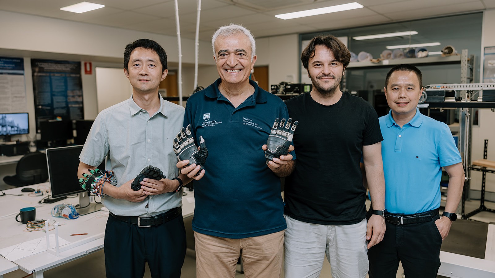 4 researchers stand in a lab, one is holding prosthetic hands and another has wires attached to his arm