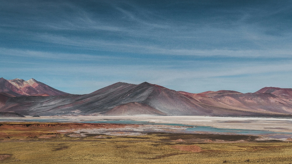 A surreal high altitude mountain and lake landscape full of blue, red and yellow colors in the desert of San Pedro de Atacama, Chile - by Jan Kronies. Credit: Unsplash