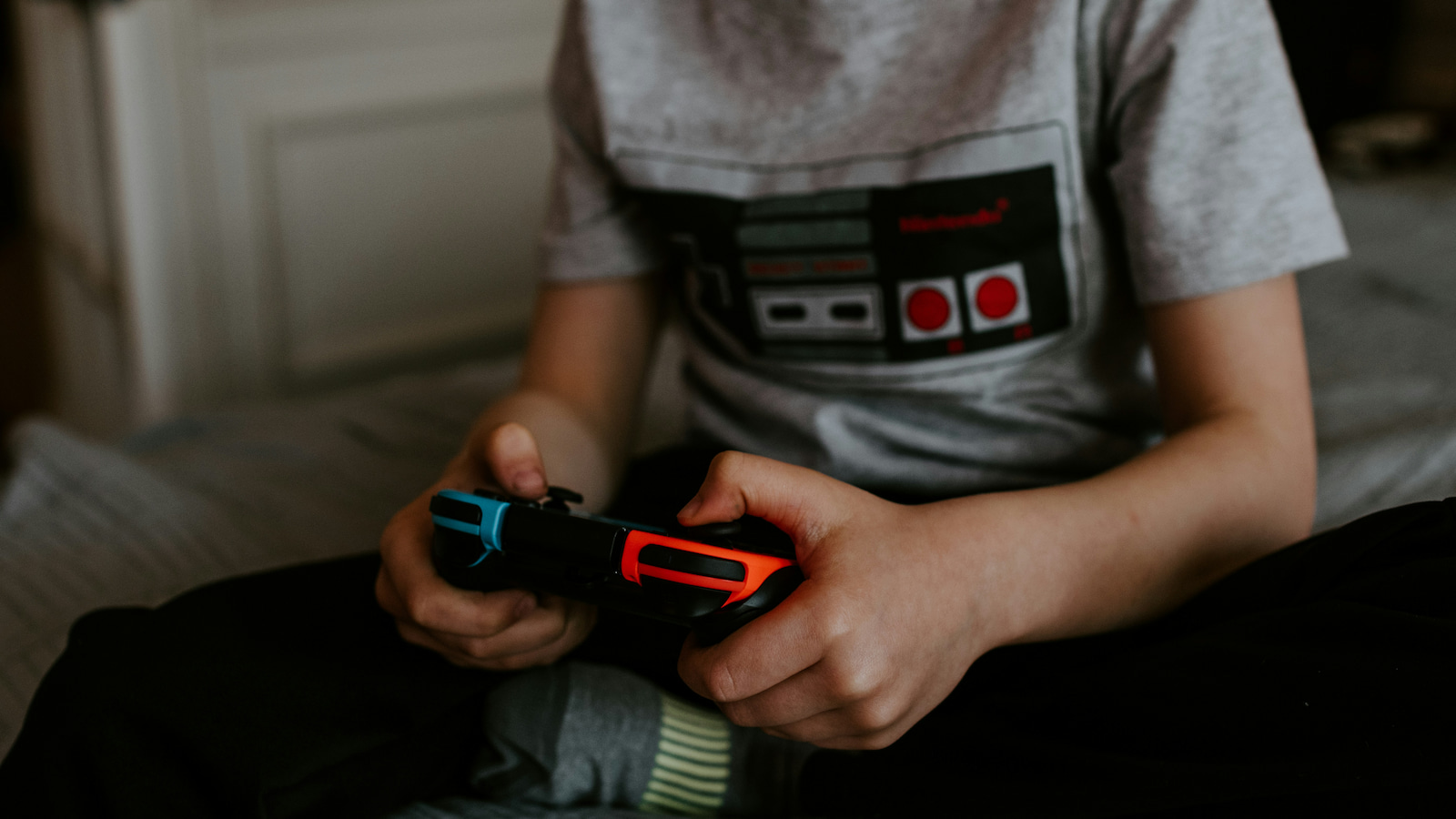 A child sits on a bed playing a Nintendo Switch. Photo: Kelly Sikkema/Unsplash