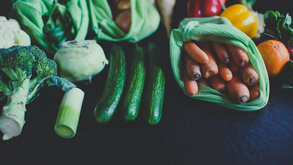 A range of fresh vegetables is displayed in reusable grocery bags on a table. Photo: Unsplash