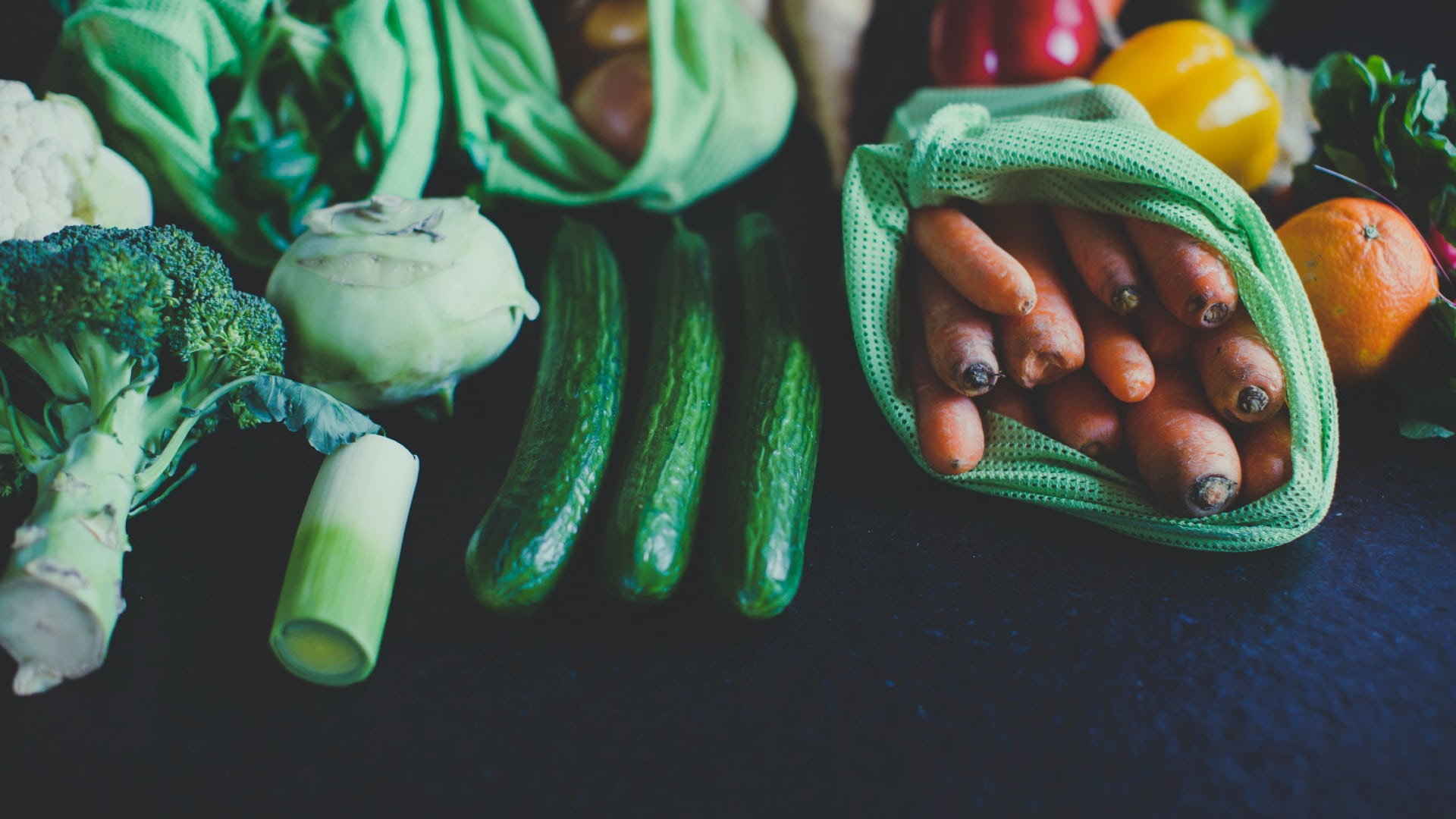 A range of fresh vegetables is displayed in reusable grocery bags on a table. Photo: Unsplash