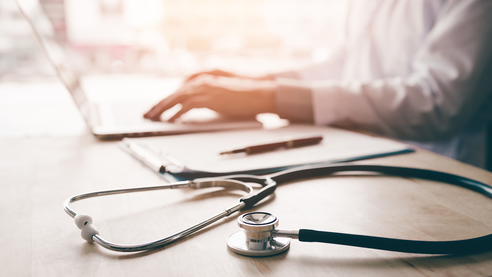 A stehoscope in the foreground with a healthcare practitioner