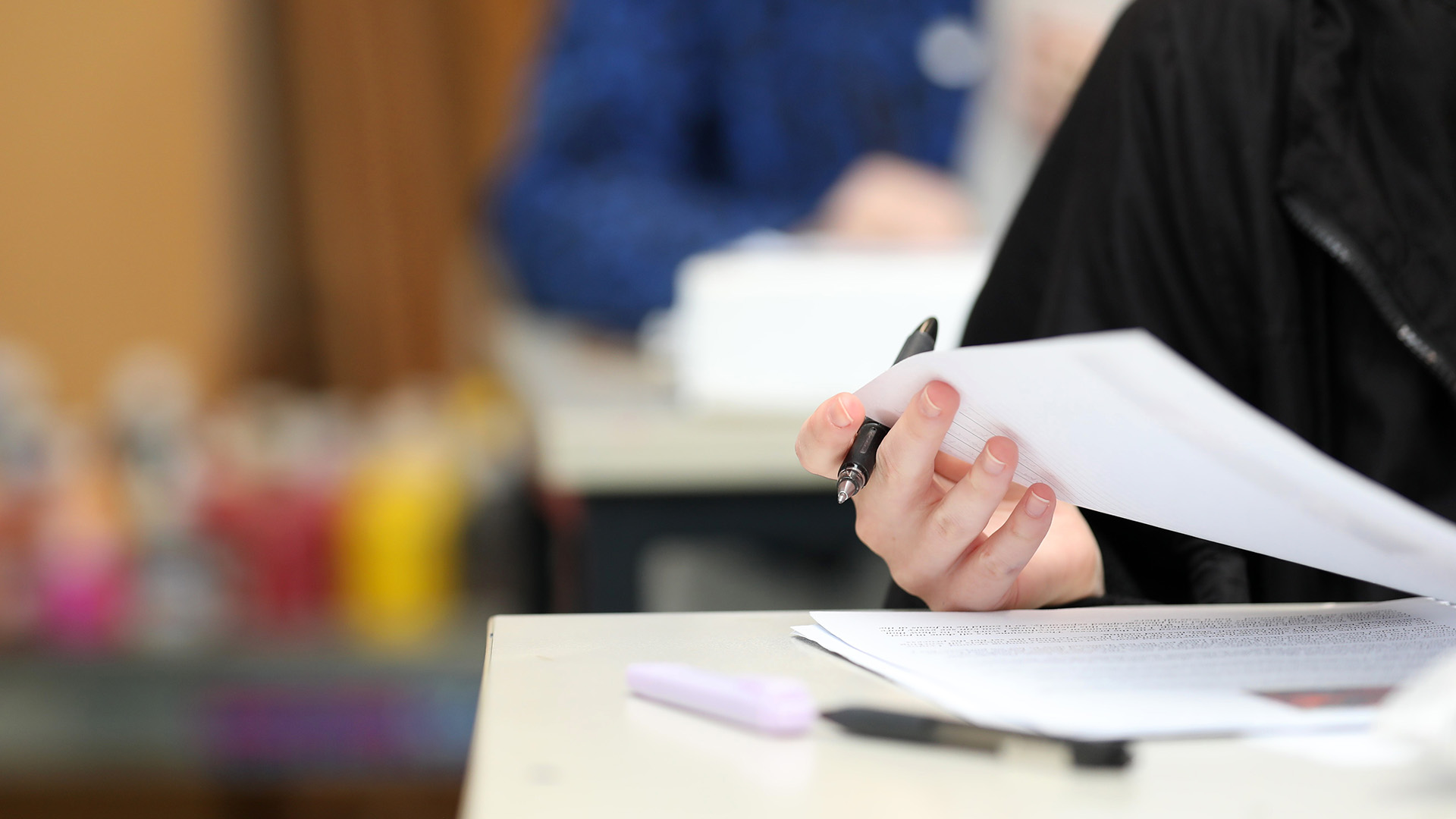 A close up isolated students hand holding a pen checking their answers during class, exam or lesson time at school. Shutterstock