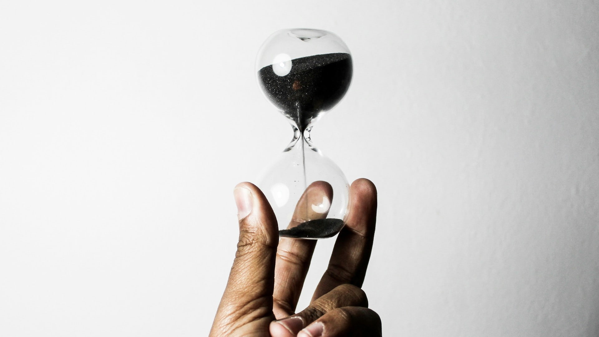 A hand holds an hourglass with black sand. Photo: Unsplash