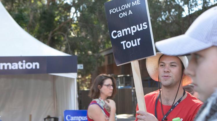 Current student holding sign which says "Follow me on a campus tour" 